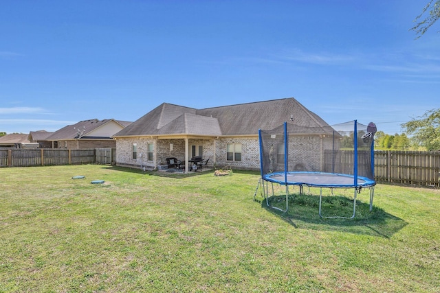 back of house featuring a lawn, a trampoline, and a fenced backyard