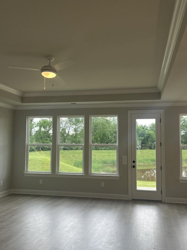 empty room with a ceiling fan, crown molding, a raised ceiling, baseboards, and wood-type flooring