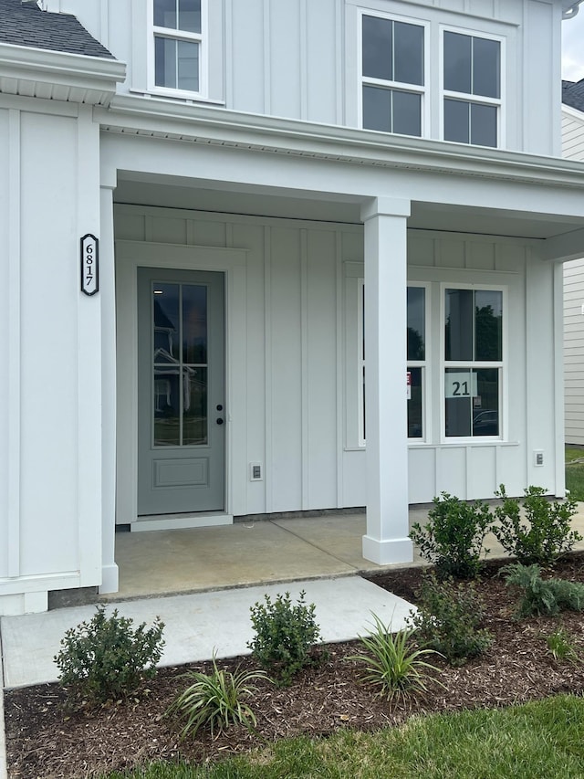 doorway to property featuring a shingled roof, board and batten siding, and covered porch