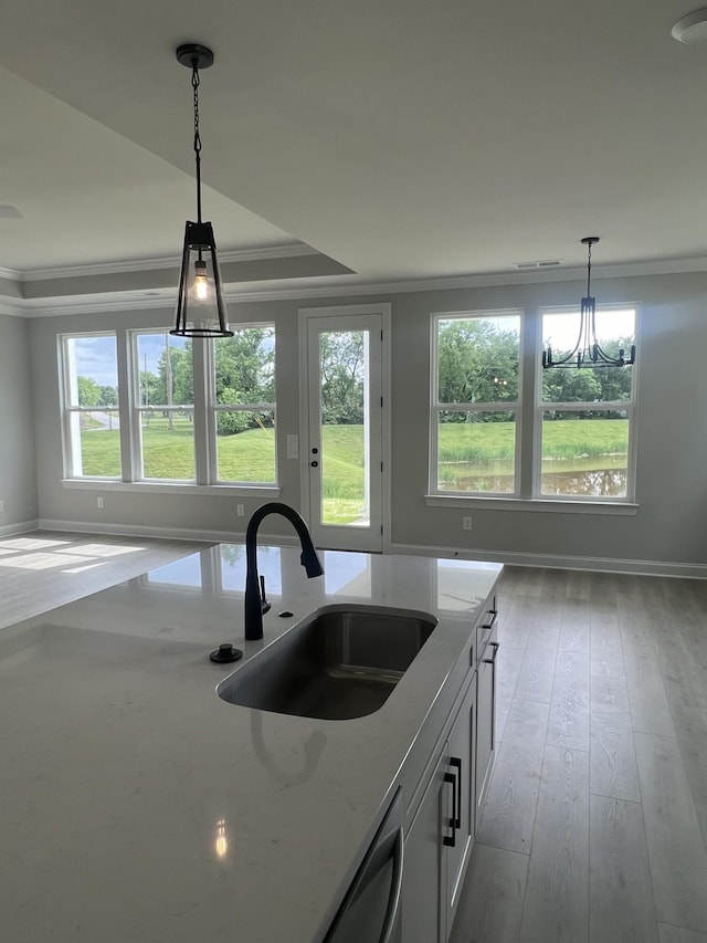 kitchen with hanging light fixtures, light stone counters, ornamental molding, and a sink