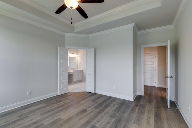 unfurnished bedroom featuring ensuite bath, baseboards, wood finished floors, a tray ceiling, and ornamental molding
