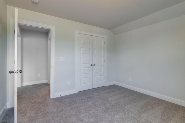 unfurnished bedroom featuring carpet floors, baseboards, a closet, and lofted ceiling