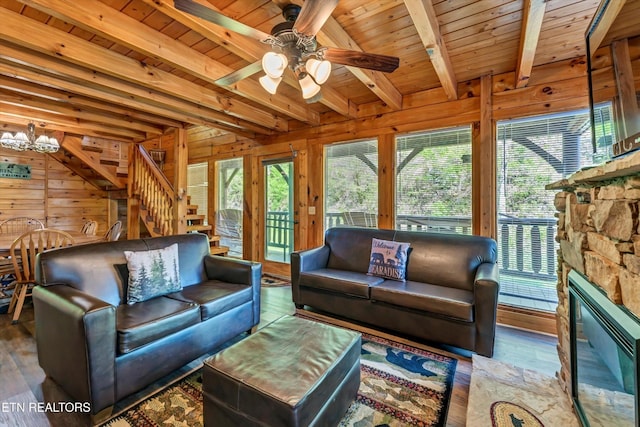 living room featuring plenty of natural light, beamed ceiling, ceiling fan with notable chandelier, and wood walls