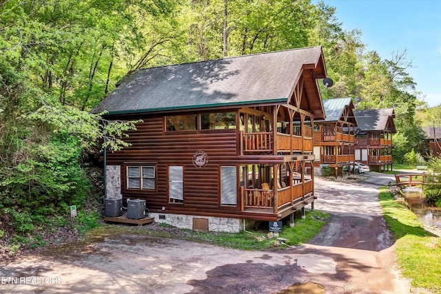 rear view of property featuring central air condition unit, a shingled roof, faux log siding, and driveway