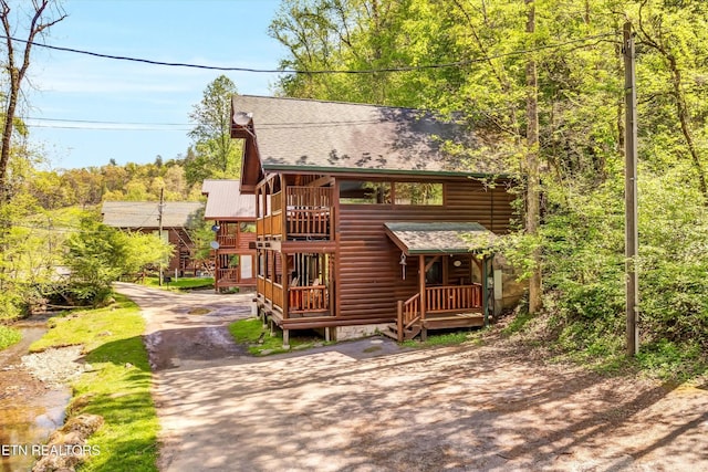 log home featuring a shingled roof, faux log siding, and driveway