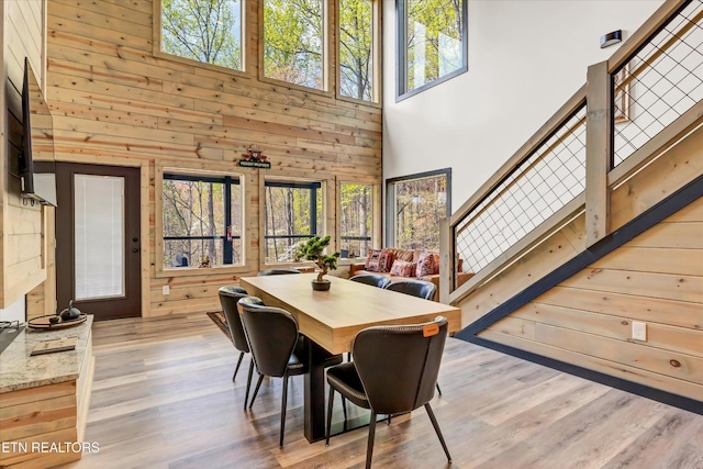 dining space featuring wooden walls, a towering ceiling, stairs, and a wealth of natural light