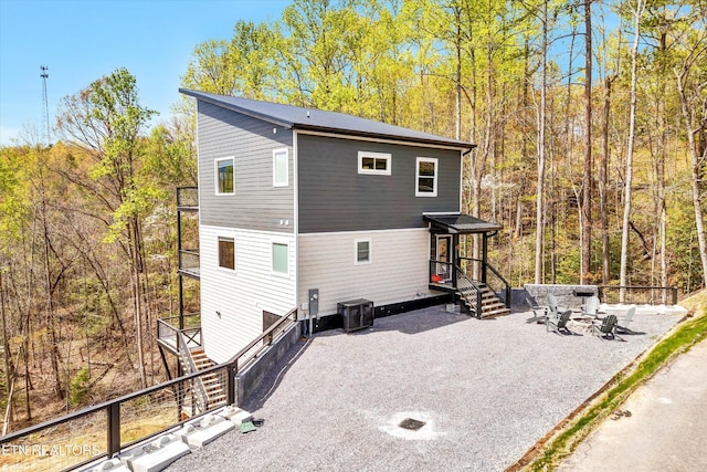 back of house with central AC unit, an outdoor fire pit, stairway, and a forest view