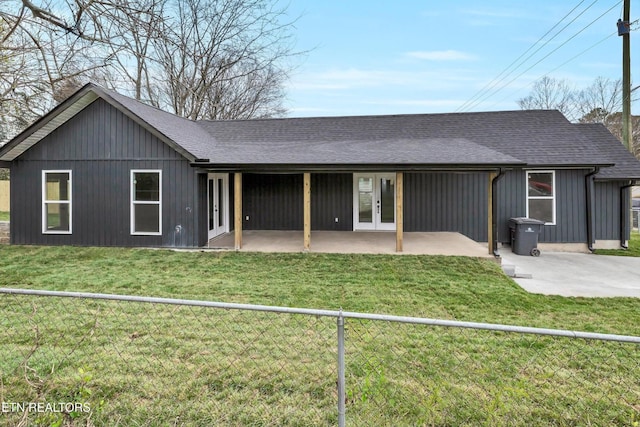 back of property with french doors, roof with shingles, a fenced backyard, a yard, and a patio