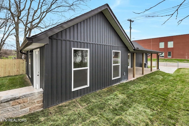 view of side of home with board and batten siding, a patio area, a yard, and fence