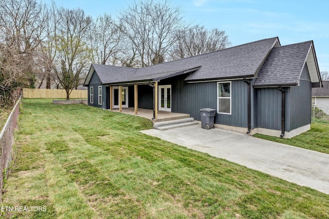 view of front of house featuring roof with shingles, fence, french doors, and a front yard