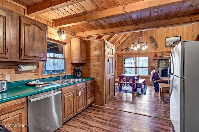 kitchen featuring wood walls, wood finished floors, a sink, beamed ceiling, and stainless steel appliances