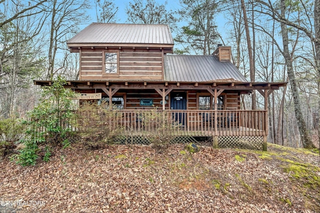 rear view of property with covered porch, a chimney, and metal roof