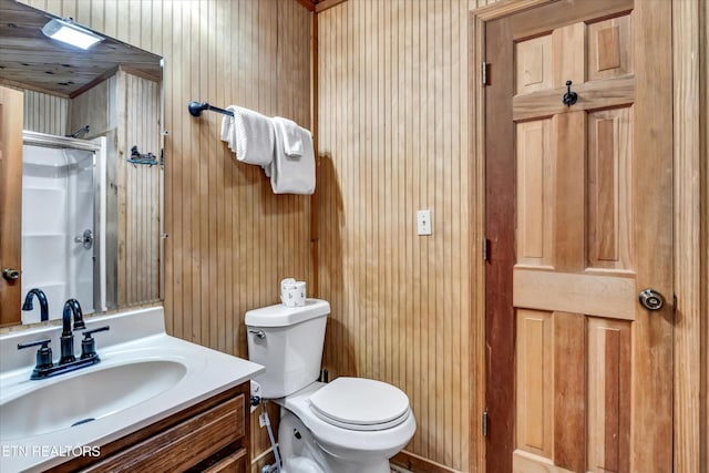 bathroom with vanity, a shower with door, wooden walls, and toilet