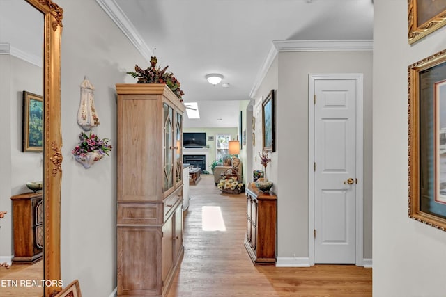 hallway featuring crown molding, light wood finished floors, and baseboards