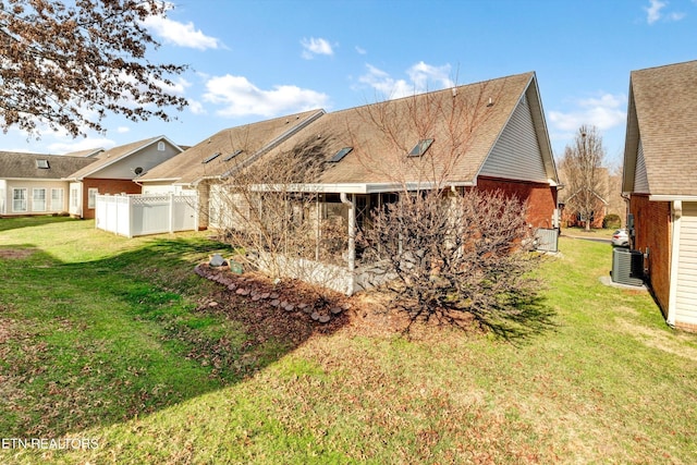 rear view of house with fence, central AC unit, a yard, and brick siding