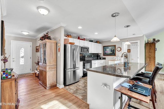 kitchen featuring appliances with stainless steel finishes, a sink, ornamental molding, a breakfast bar, and white cabinetry