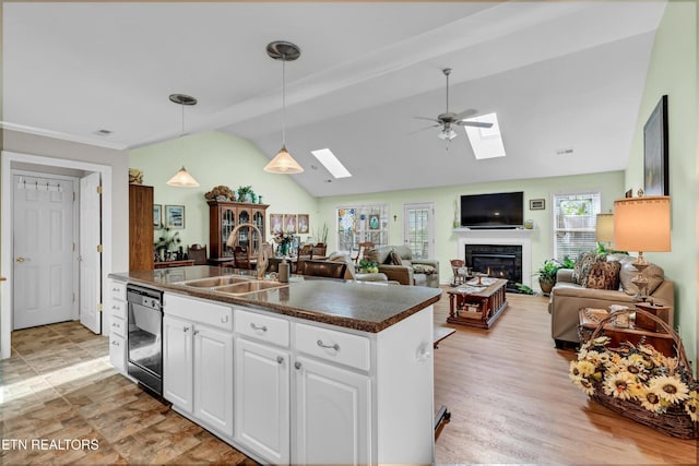 kitchen with dark countertops, black dishwasher, white cabinets, vaulted ceiling with skylight, and a sink
