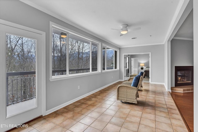sitting room with baseboards, crown molding, a glass covered fireplace, and ceiling fan