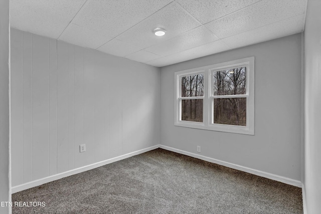 empty room with baseboards, dark carpet, and a paneled ceiling