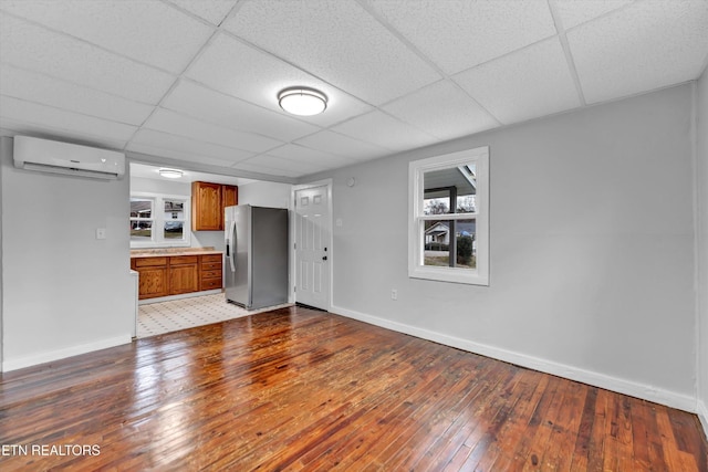 unfurnished living room with a paneled ceiling, baseboards, light wood-style flooring, and a wall mounted air conditioner