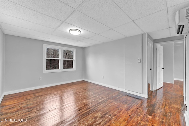 spare room with baseboards, a wall mounted AC, a drop ceiling, and hardwood / wood-style floors