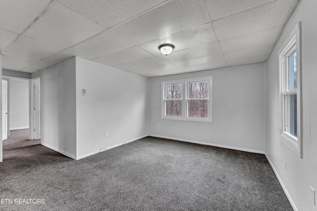empty room featuring baseboards, dark carpet, and a paneled ceiling