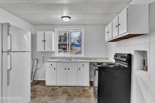 kitchen with black / electric stove, a sink, white cabinets, freestanding refrigerator, and a drop ceiling