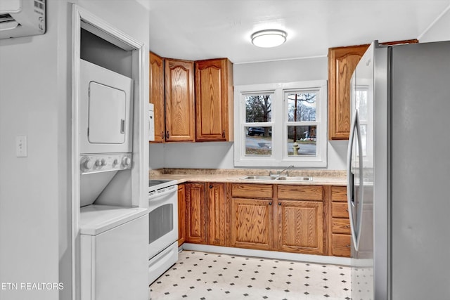 kitchen with stacked washer / dryer, brown cabinets, a sink, freestanding refrigerator, and white electric range oven