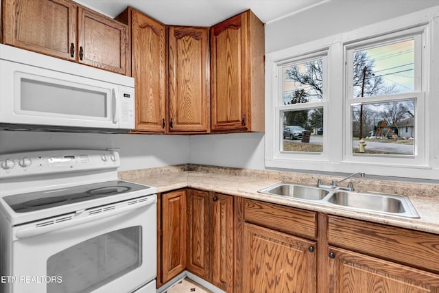kitchen featuring a sink, brown cabinets, white appliances, and light countertops