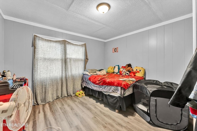 bedroom featuring ornamental molding, a textured ceiling, a decorative wall, and wood finished floors