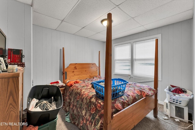 bedroom with wooden walls, a drop ceiling, and carpet