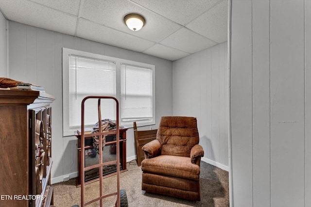 living area featuring baseboards, a drop ceiling, and carpet flooring