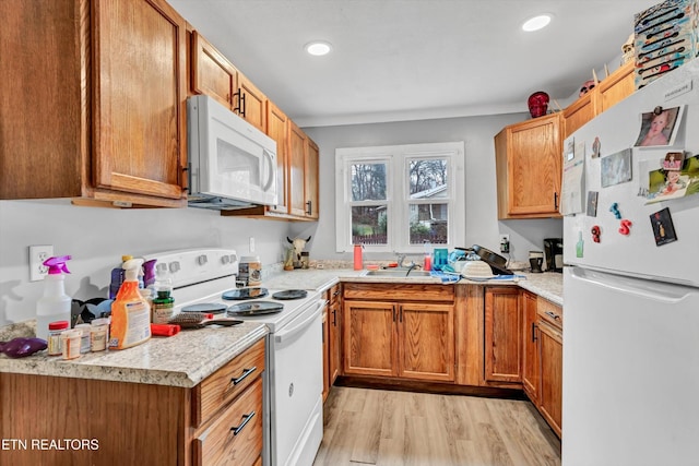 kitchen featuring white appliances, recessed lighting, light countertops, a sink, and light wood finished floors