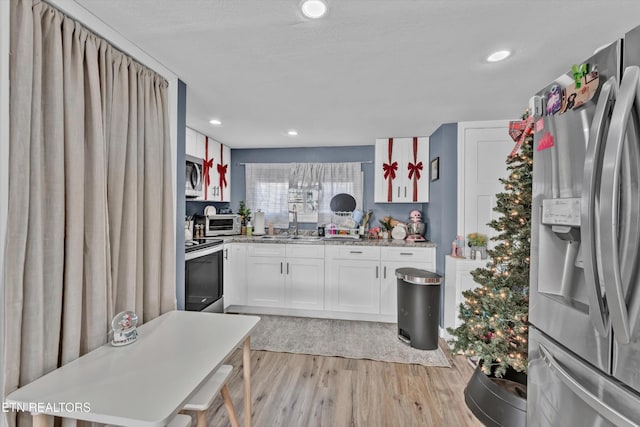 kitchen with light wood-type flooring, recessed lighting, white cabinets, a sink, and appliances with stainless steel finishes