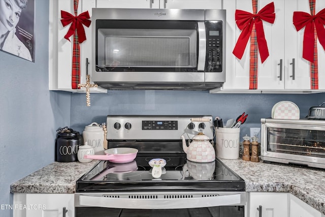 kitchen featuring a textured wall, electric range, a toaster, white cabinetry, and stainless steel microwave