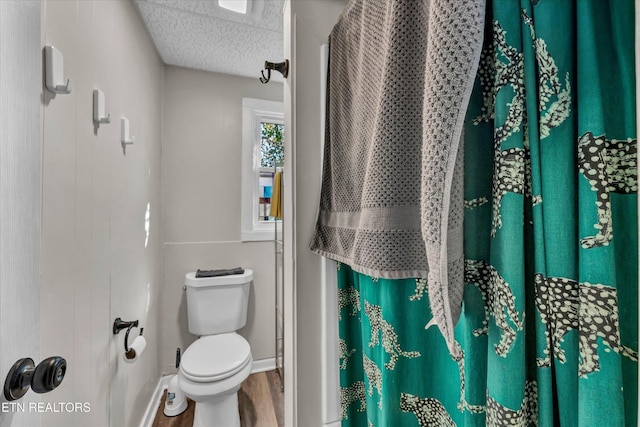 full bath featuring a shower with curtain, a textured ceiling, wood finished floors, baseboards, and toilet