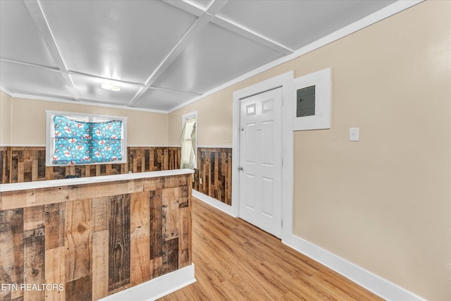 interior space with wainscoting, wood walls, baseboards, coffered ceiling, and light wood-style flooring