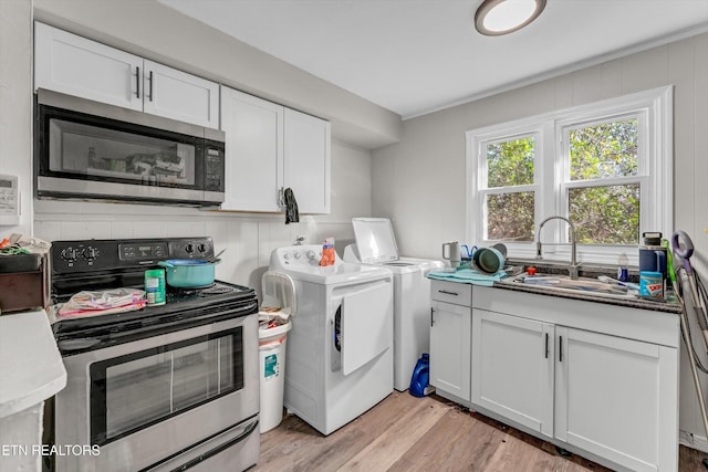 kitchen with appliances with stainless steel finishes, a sink, light wood-style flooring, white cabinetry, and washing machine and dryer