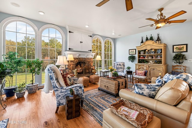 living area featuring plenty of natural light, a ceiling fan, light wood finished floors, and a stone fireplace