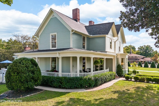 view of front of property with roof with shingles, a chimney, a porch, and a front lawn