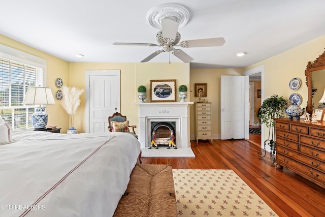 bedroom with ceiling fan, a fireplace, and wood finished floors