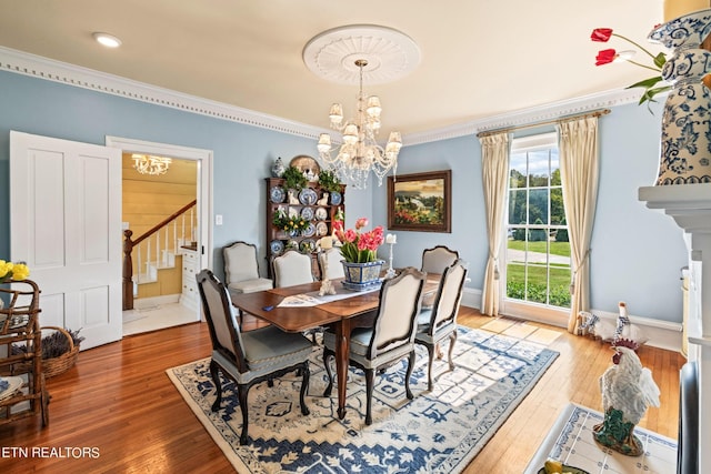 dining room with an inviting chandelier, hardwood / wood-style flooring, crown molding, and stairs