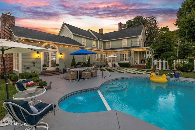 rear view of house featuring fence, a fenced in pool, a chimney, french doors, and a patio