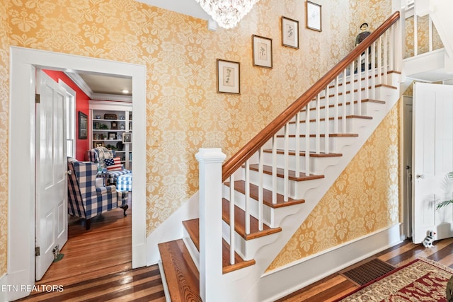 stairway featuring visible vents, crown molding, wood finished floors, wallpapered walls, and a chandelier