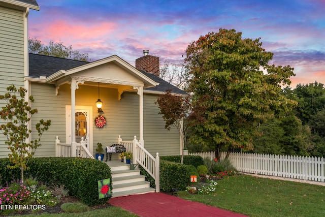 view of front of home with fence, roof with shingles, a front lawn, a porch, and a chimney