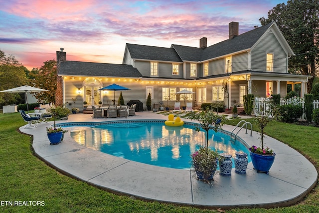 rear view of house with a lawn, an outdoor pool, a chimney, and a patio