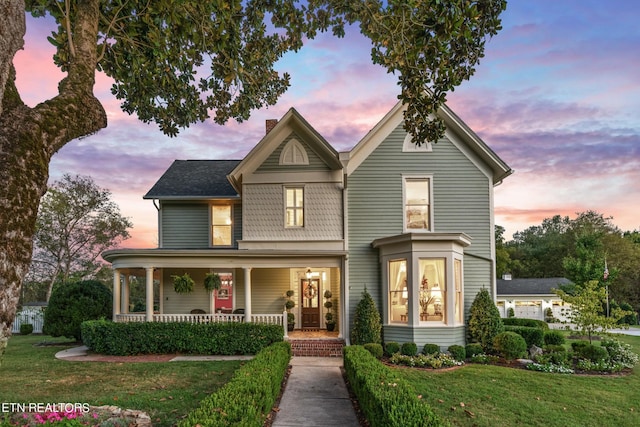 victorian house featuring a lawn, covered porch, and a chimney