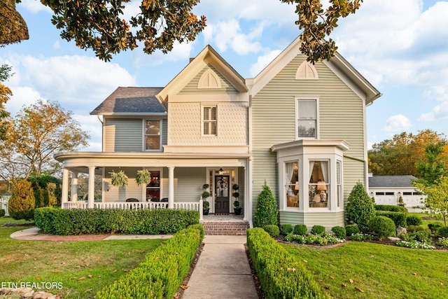 view of front of home featuring roof with shingles, a porch, and a front lawn
