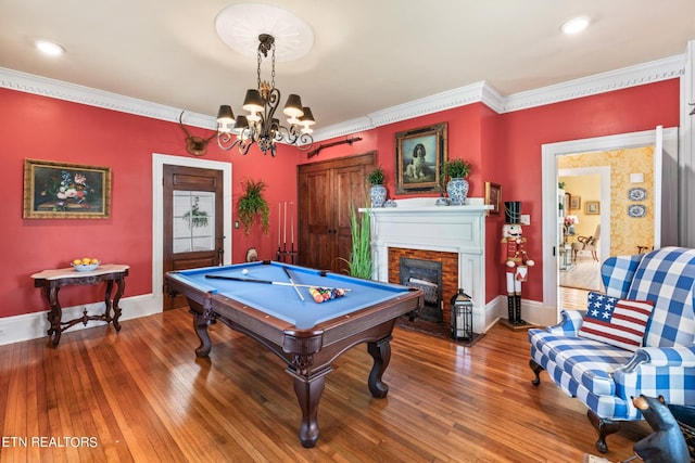 recreation room featuring ornamental molding, wood finished floors, a fireplace, pool table, and a chandelier