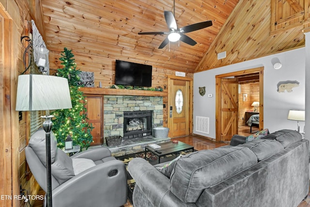 living room with wood walls, a stone fireplace, a ceiling fan, visible vents, and wood ceiling